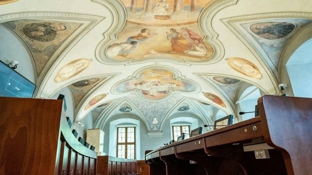 Sala sesyjna Rady Miasta Poznania, pusta, widoczne stanowiska radnych i zdobiące sufit zabytkowe freski - grafika artykułu