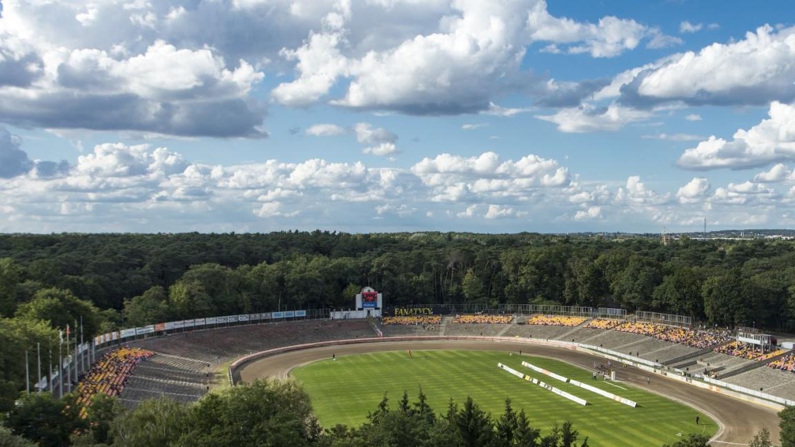 widok z lotu ptaka na stadion żużlowy otoczony gęstą zielenią drzewami - grafika artykułu