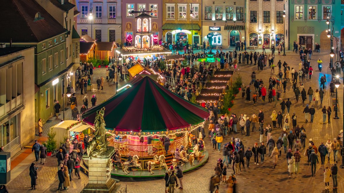 XIX wieczna kolorowa karuzela na płycie Starego Rynku, obok stragany jarmarczne oraz urokliwe kamieniczki.