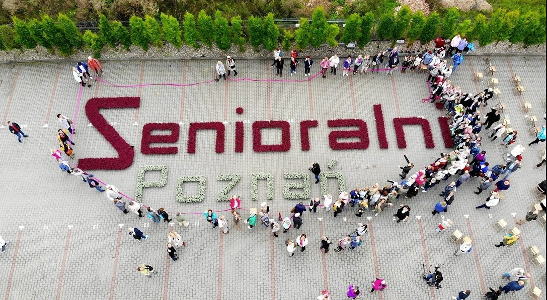 Zdjęcie z lotu ptaka, widać ludzi stojących wokół ułożonego z kwiatów napisu: Senioralni Poznań - grafika artykułu