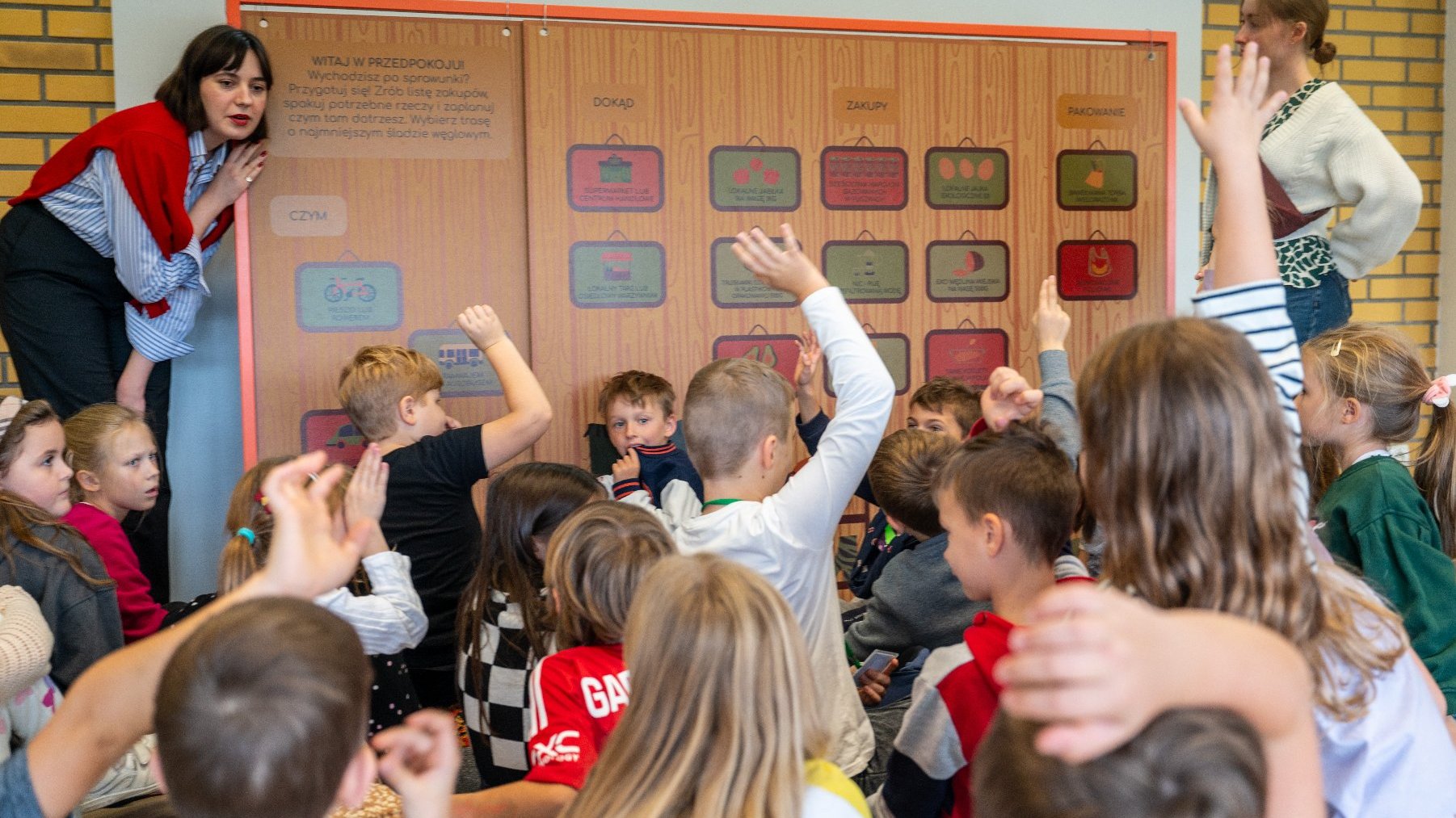 Zdjęcie przedstawia grupę dzieci i dorosłych przy tablicy edukacyjnej.