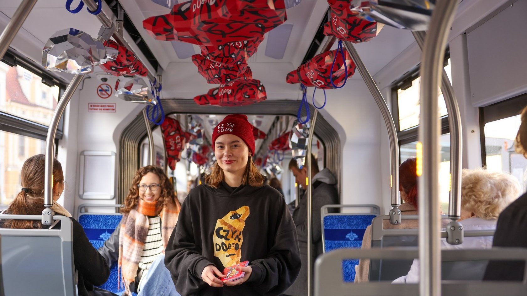 Na zdjęciu kobieta w czapce z napisem: czyń dobro w tramwaju udekorowanym rogalami