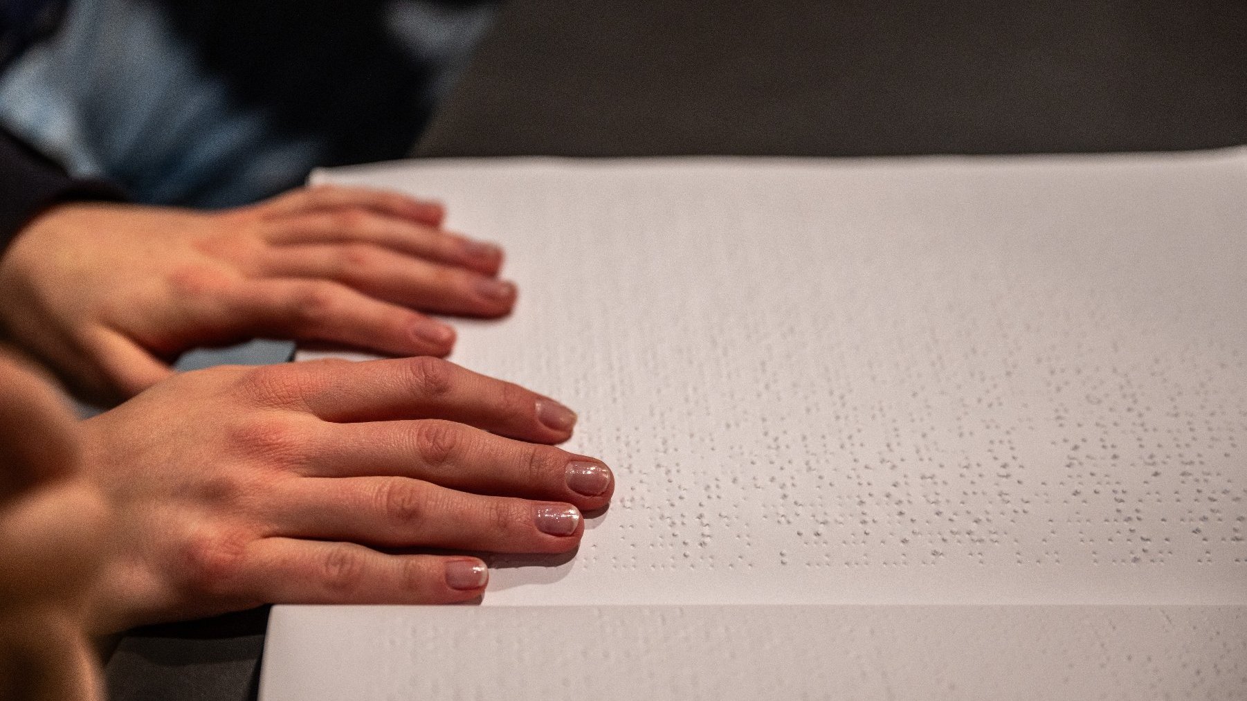 Na zdjęciu książka w alfabecie Braille'a, na niej dwie dłonie