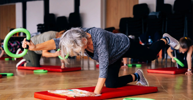Zdjęcie przedstawia seniorkę wykonującą ćwiczenia na macie.