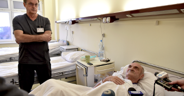 Na zdjęciu pacjent w łóżku i stojący przy nim lekarz