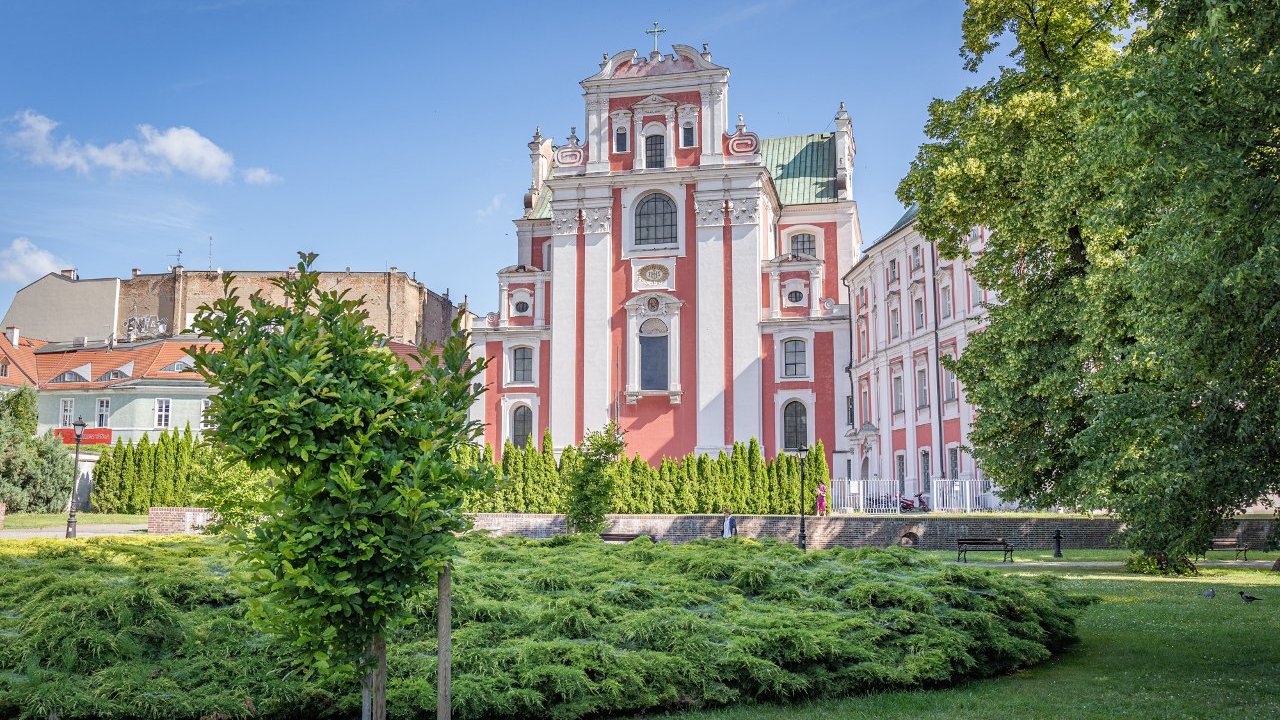 Park, trawa, drzewa, w tle biało-różowy zabytkowy budynek