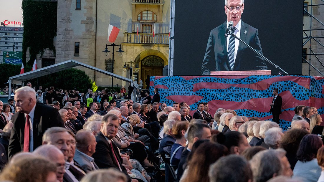 Telebim, ludzie siedzą na krzesłach.