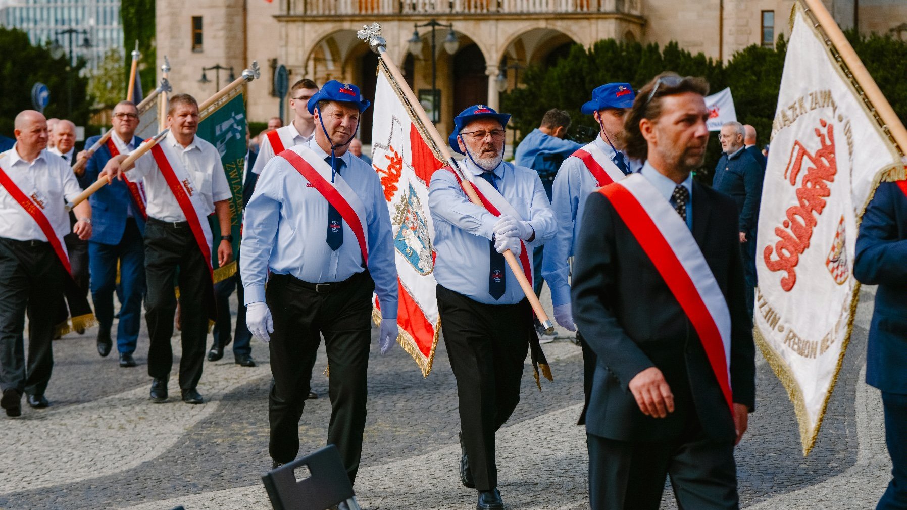 Zdjęcie przedstawia ludzi idących z flagami.