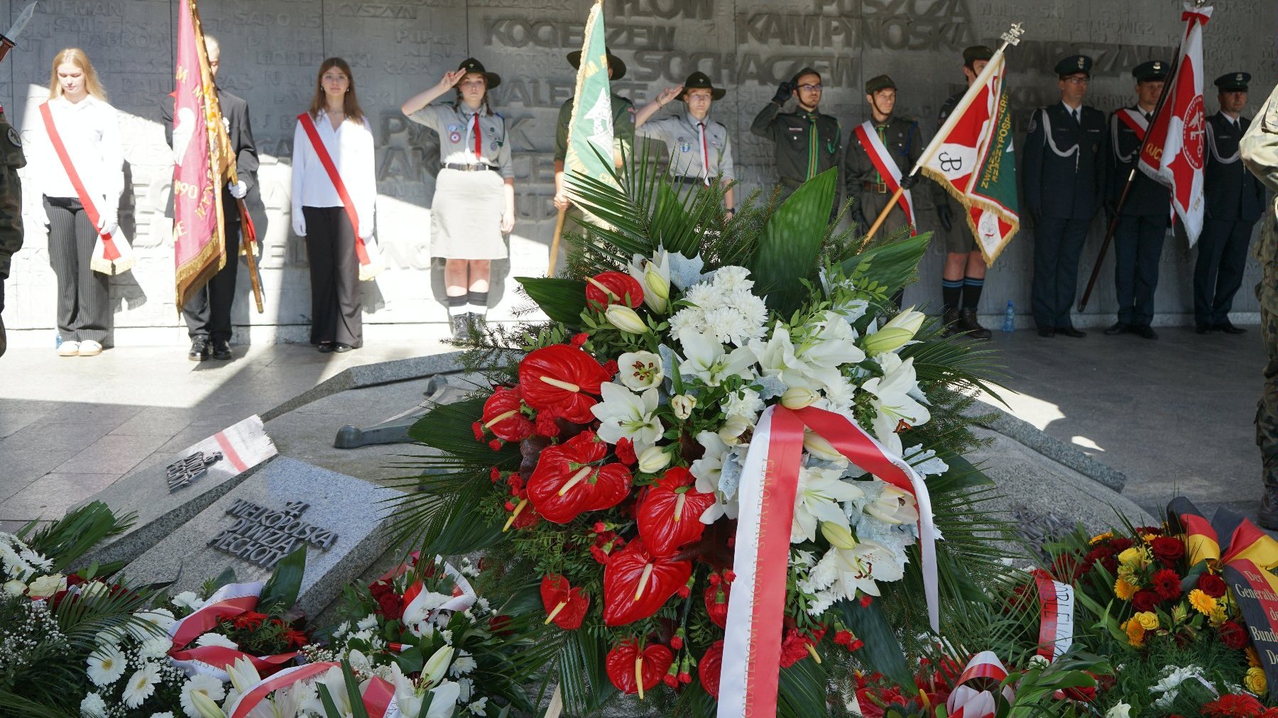 Na zdjęciu pomnik Armii Poznań, przy nim kwiaty, w tle salutujące poczty sztandarowe