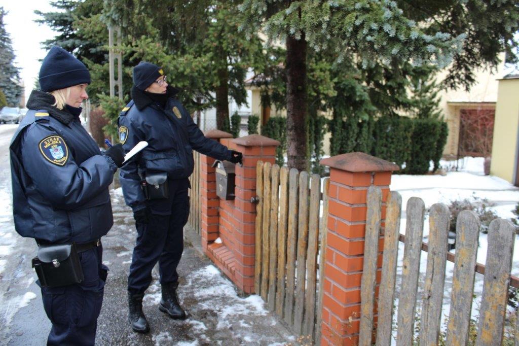 Zdjęcie przedstawia dwie strażniczki miejskie, które stoją przed wejściem na posesję. Jedna z nich robi notatki, druga wskazuje na furtkę. - grafika artykułu