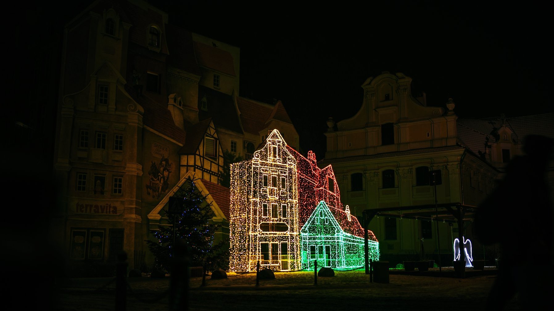 Zdjęcie przedstawia budynki. Na jednym z nich znajduje się mural. Widać też iluminację w kształcie budynków.