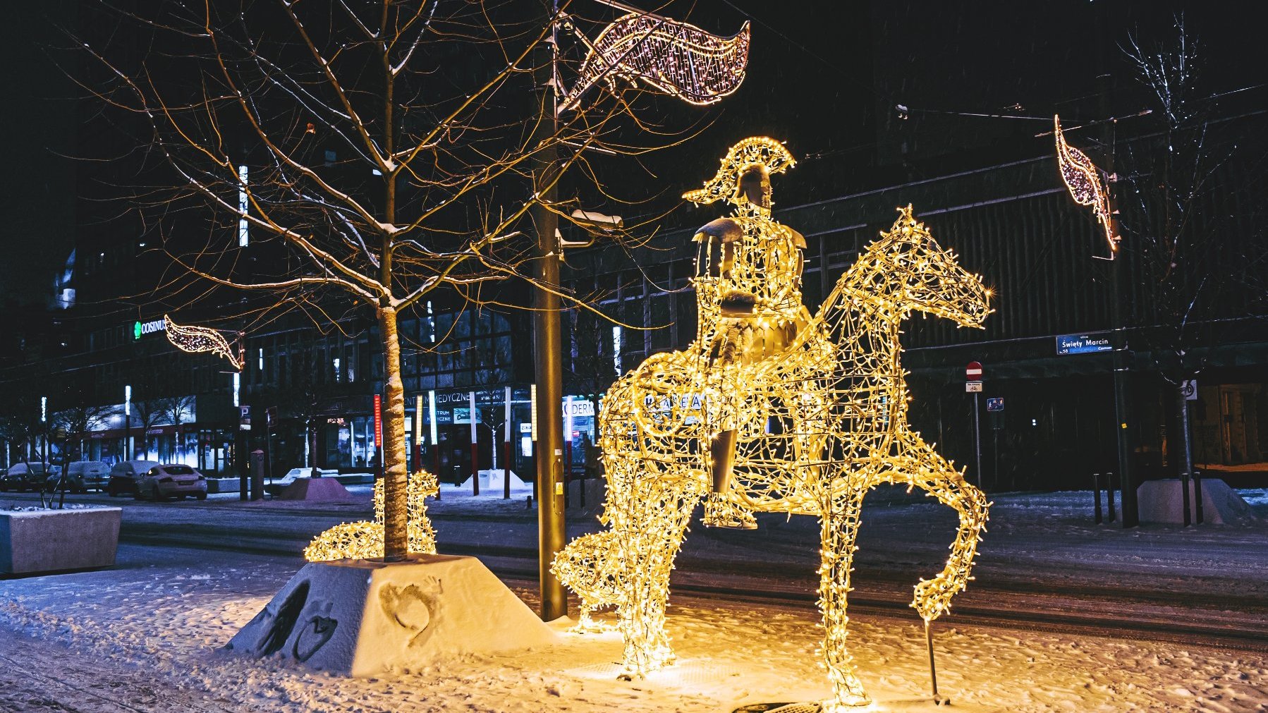 Zdjęcie przedstawia iluminację w kształcie Świętego Marcina na koniu. Iluminacja znajduje się na ulicy. W tle widać witryny sklepów.