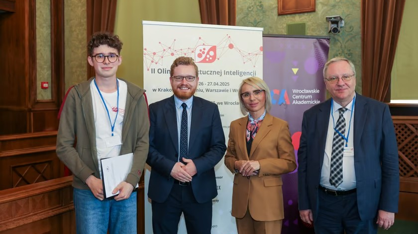 W gronie ósemki laureatów, którzy pojadą na Międzynarodową Olimpiadę Sztucznej Inteligencji w Pekinie, znalazł się Jan Kociszewski - uczeń II LO w Poznaniu Cztery osoby stojące obok siebie na tle banera informującego o II Olimpiadzie Sztucznej Inteligencji. Od lewej: młody mężczyzna w okularach i jasnej bluzie z identyfikatorem na szyi, uśmiechnięty mężczyzna w garniturze z krawatem, kobieta w brązowym garniturze z chustą na szyi i okularach oraz starszy mężczyzna w garniturze z krawatem i okularach. W tle po prawej widoczne jest logo Wrocławskiego Centrum Akademickiego.