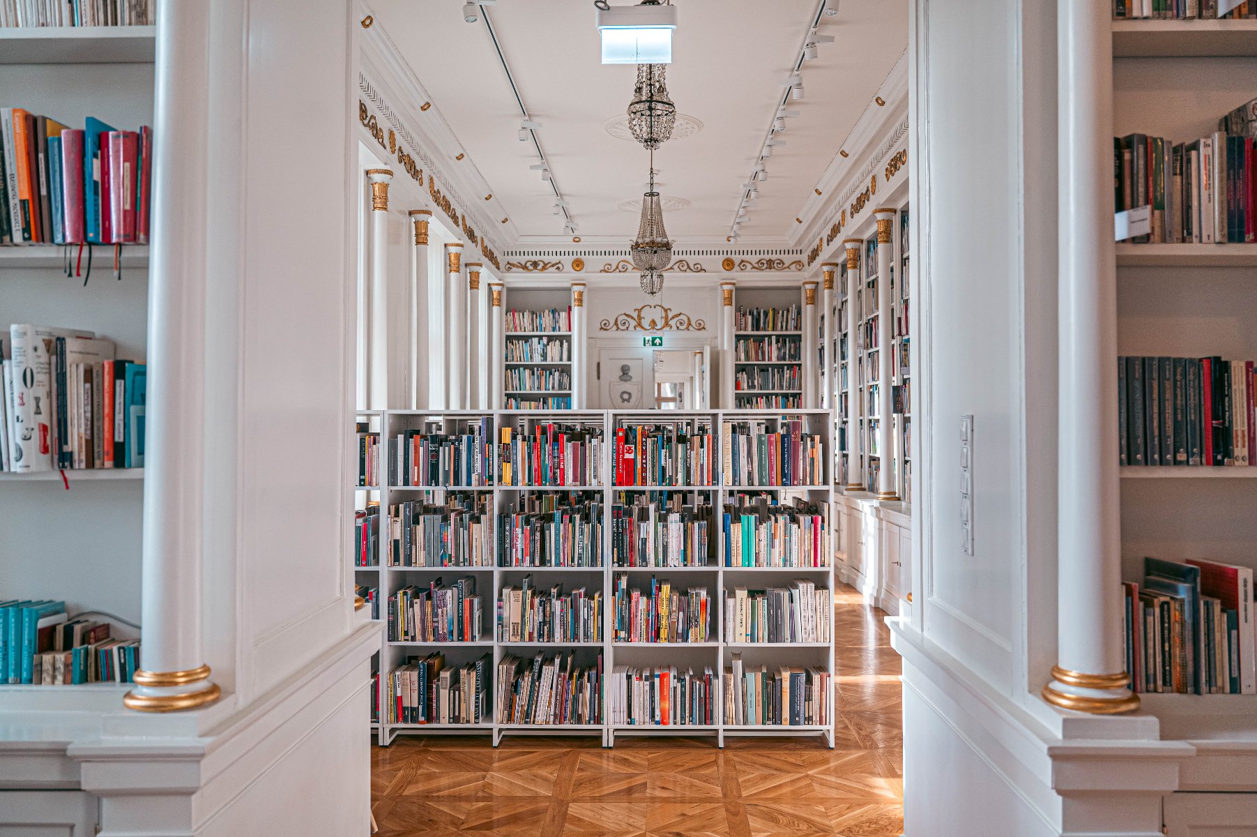 W sobotę, 23 sierpnia w Filii Sztuki Biblioteki Raczyńskich odbędą się kolejne CZYTATY 9 muz Eleganckie wnętrze biblioteki, pełne białych regałów z książkami. Na podłodze widać drewniany parkiet. Na suficie wiszą żyrandole, a na ścianach są złote detale.