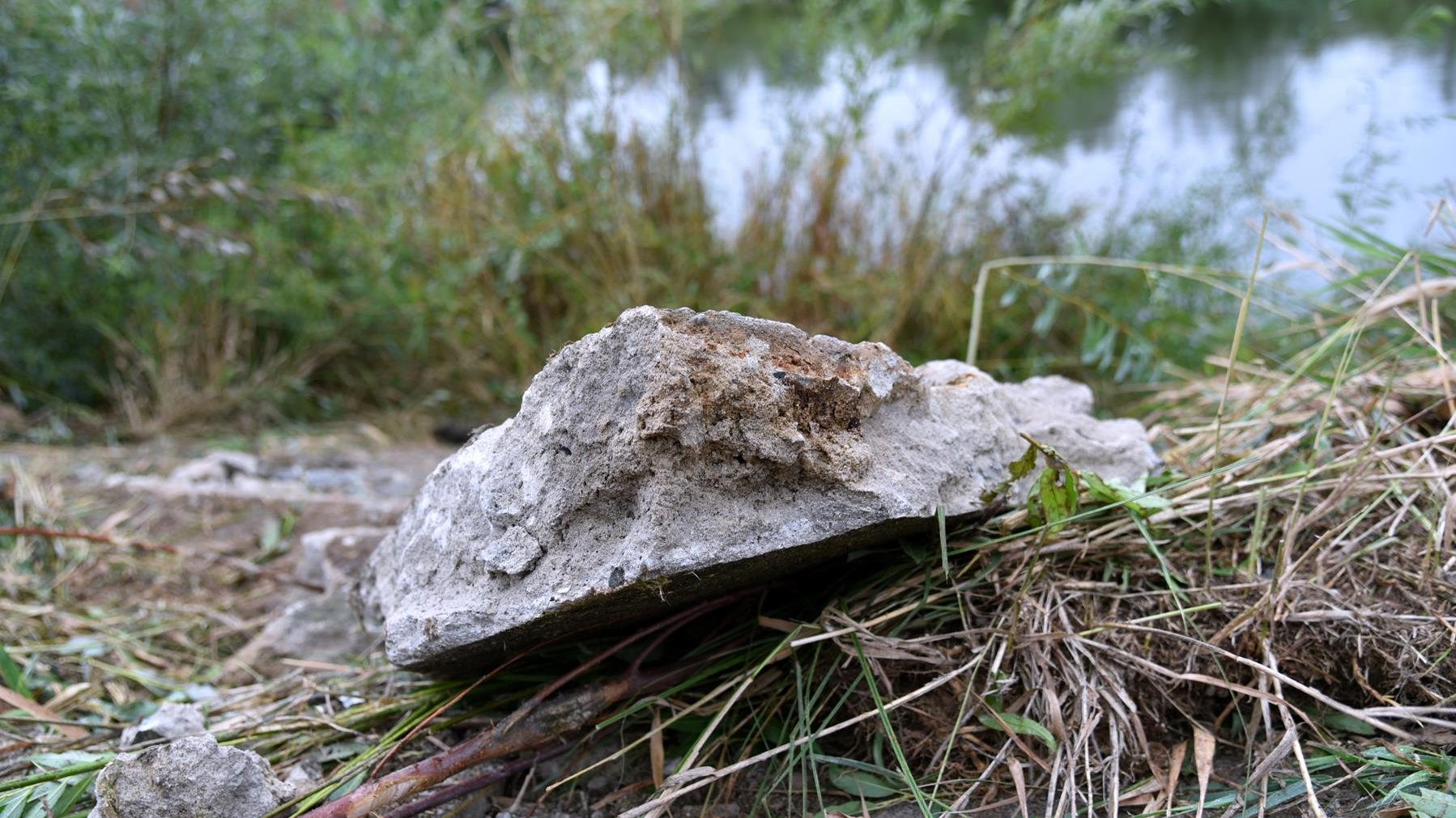 Zdjęcie przedstawia fragment betonowego umocnienia rzeki, w tle widać Wartę