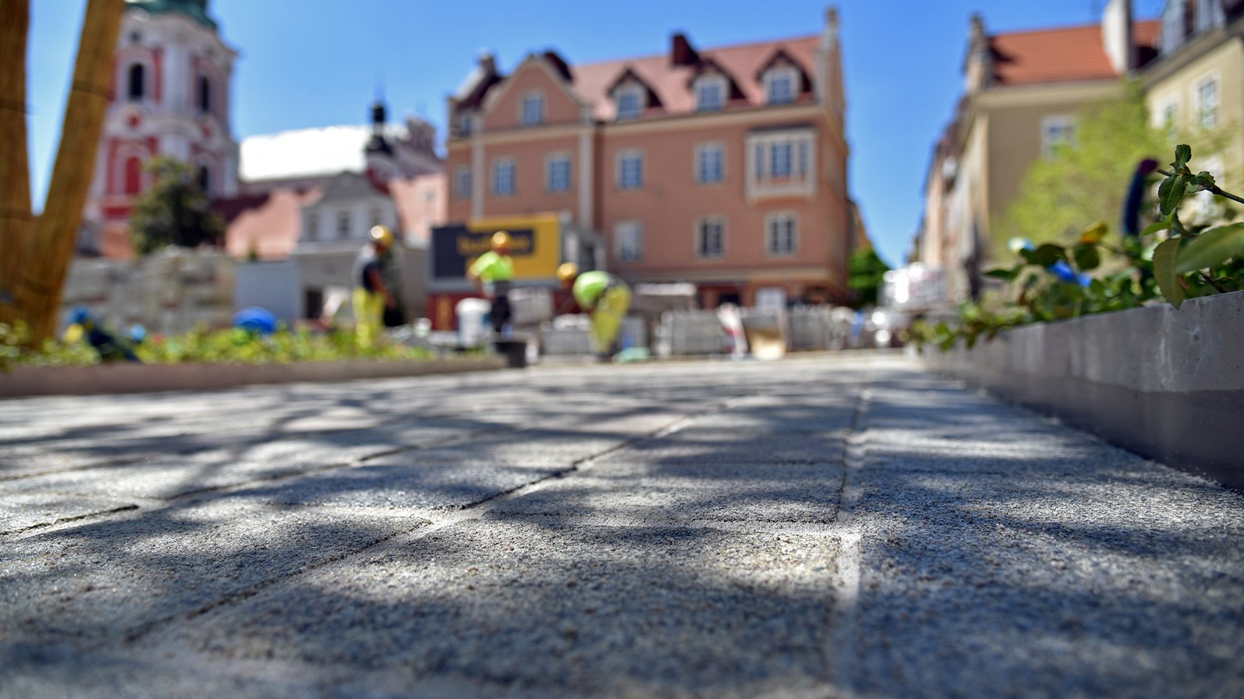 zbliżenie na kamienną nawierzchnię. W tle budynki wokół placu Kolegiackiego i wieża kościoła