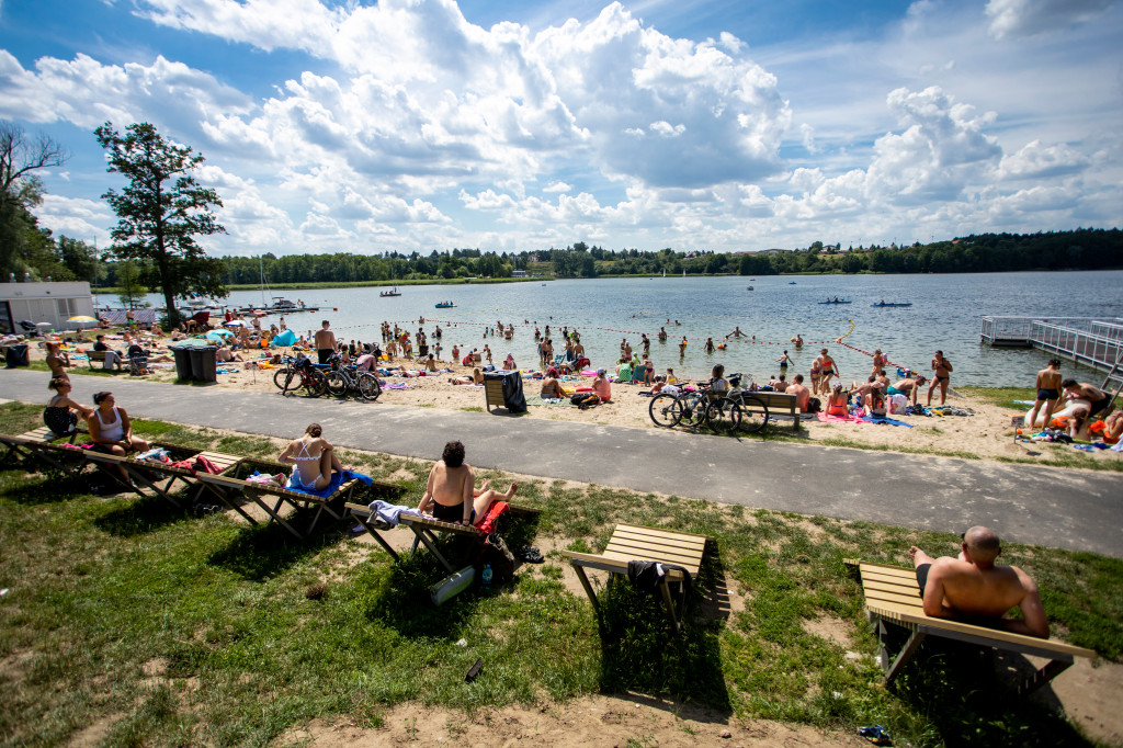 Zdjęcie przedstawia ludzi siedzących i leżących na plaży nad jeziorem. - grafika artykułu