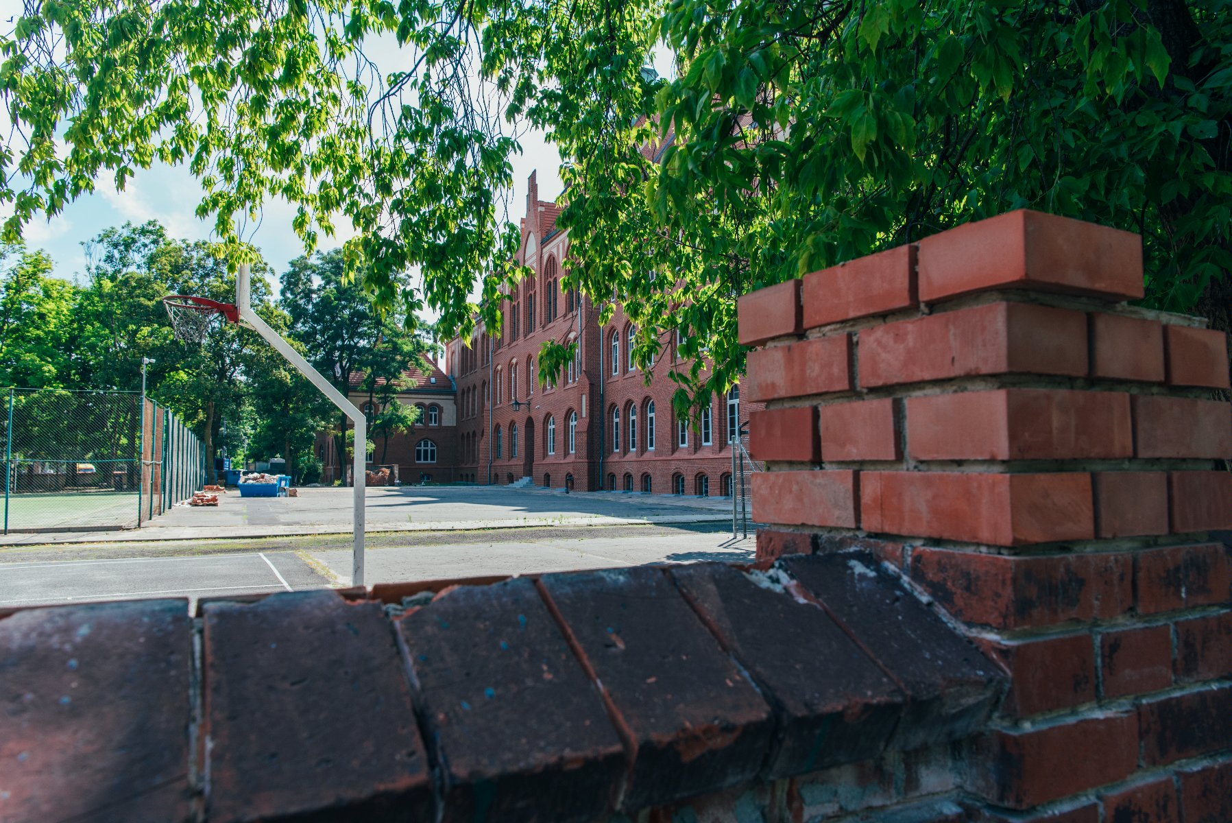 Zdjęcie przedstawia budynek szkoły, na pierwszym planie znajduje się betonowe ogrodzenie. - grafika artykułu