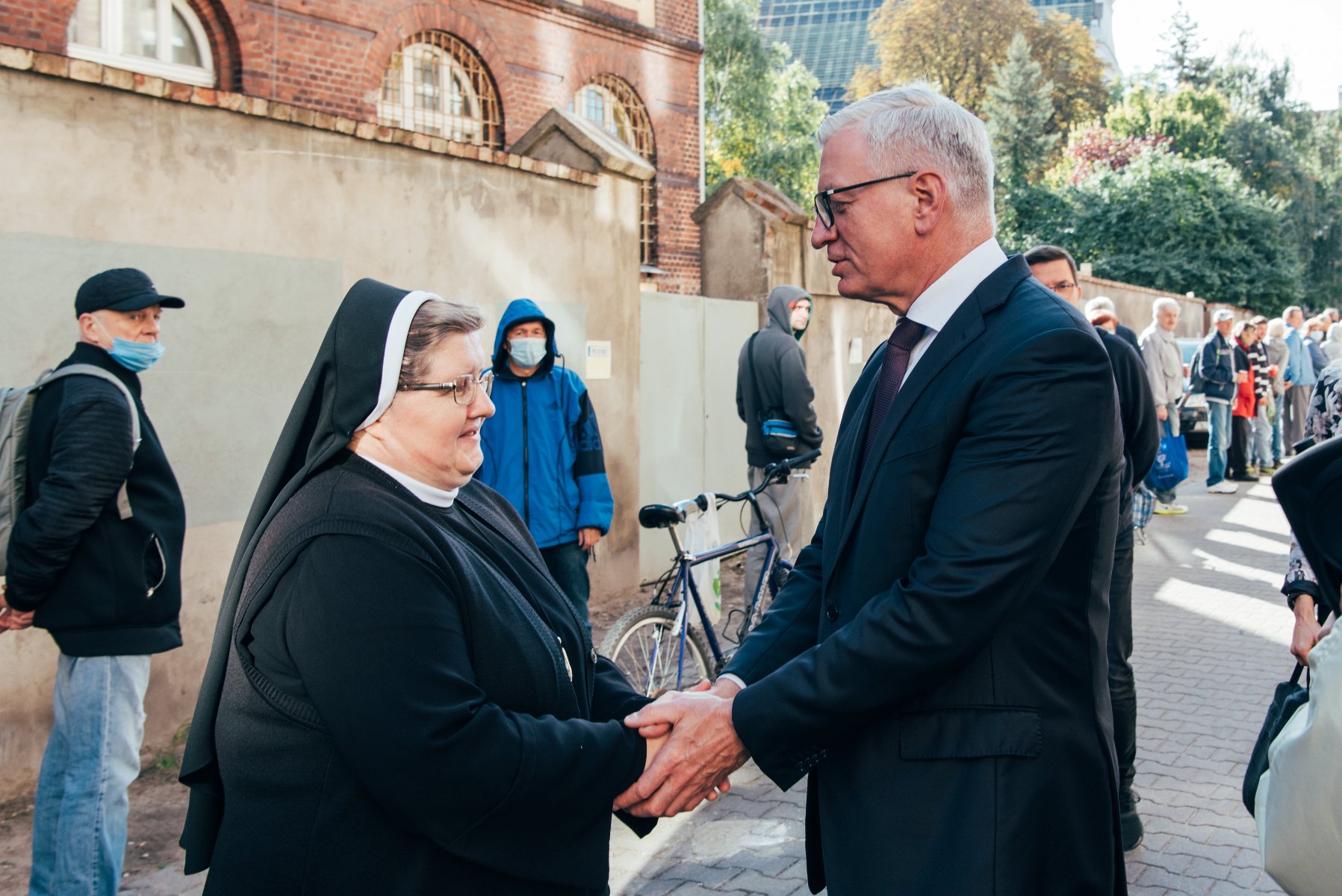 Na zdjęciu Jacek Jaśkowiak, prezydent Poznania, ściskający dłonie siostry Józefy, w tle kolejka ludzi - grafika artykułu