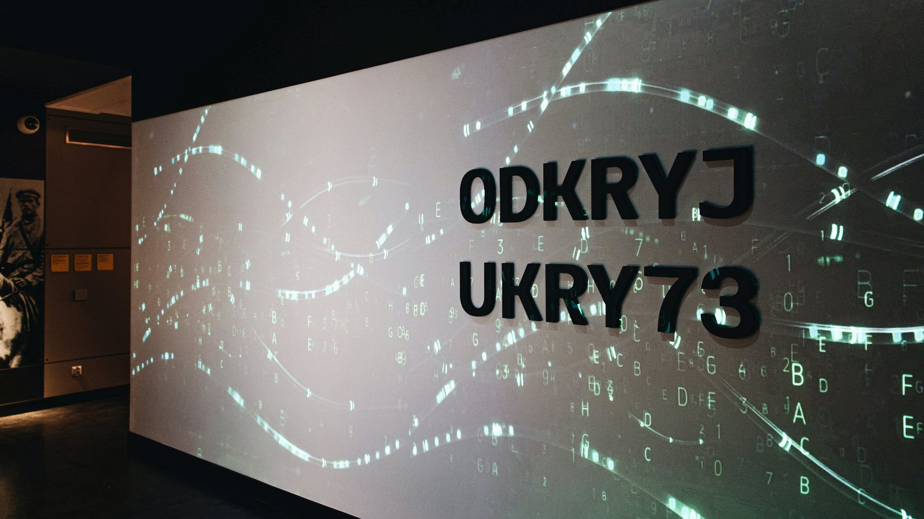 Na zdjęciu widać ekran, będący elementem multimedialnej ekspozycji Centrum, na którym wyświetla się napis "Odkryj ukryte". - grafika artykułu