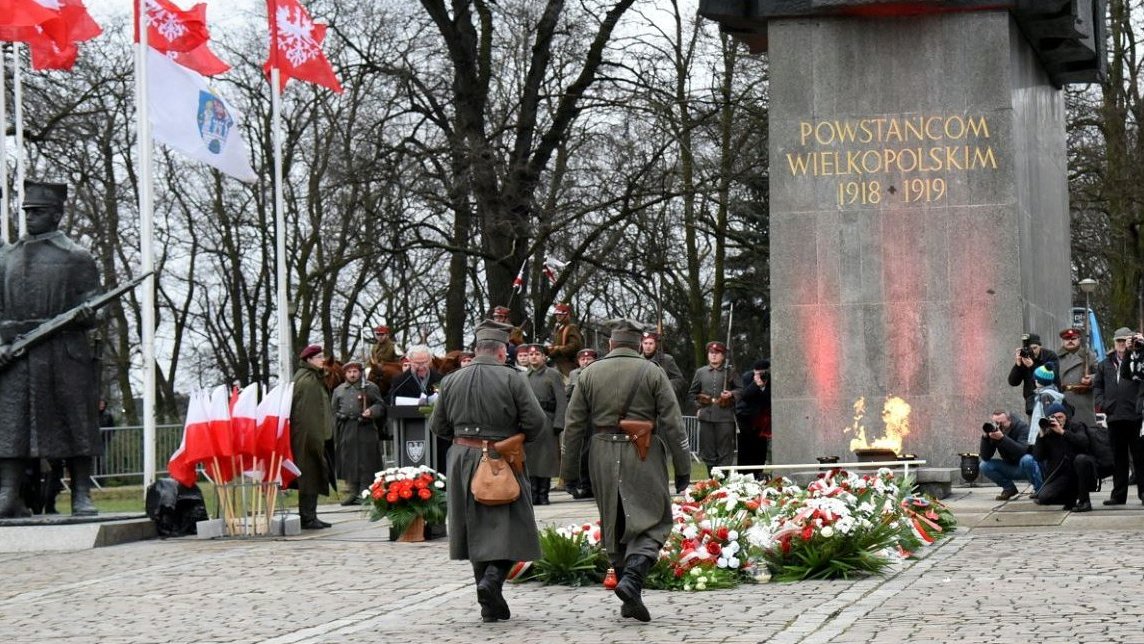 Zdjęcie przedstawia osoby składające kwiaty pod pomnikiem Powstańców Wielkopolskich.