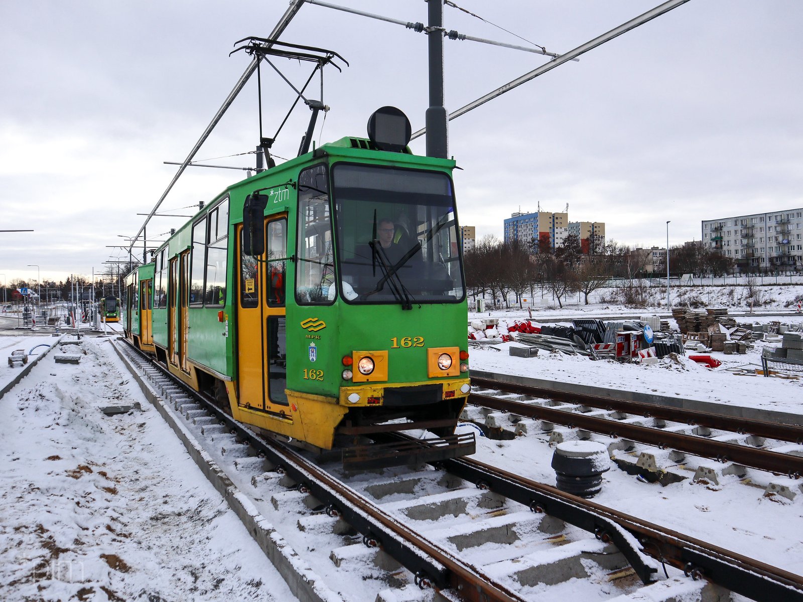 Tramwaj stojący na torowisku, w tle bloki, na trawie śnieg - grafika artykułu