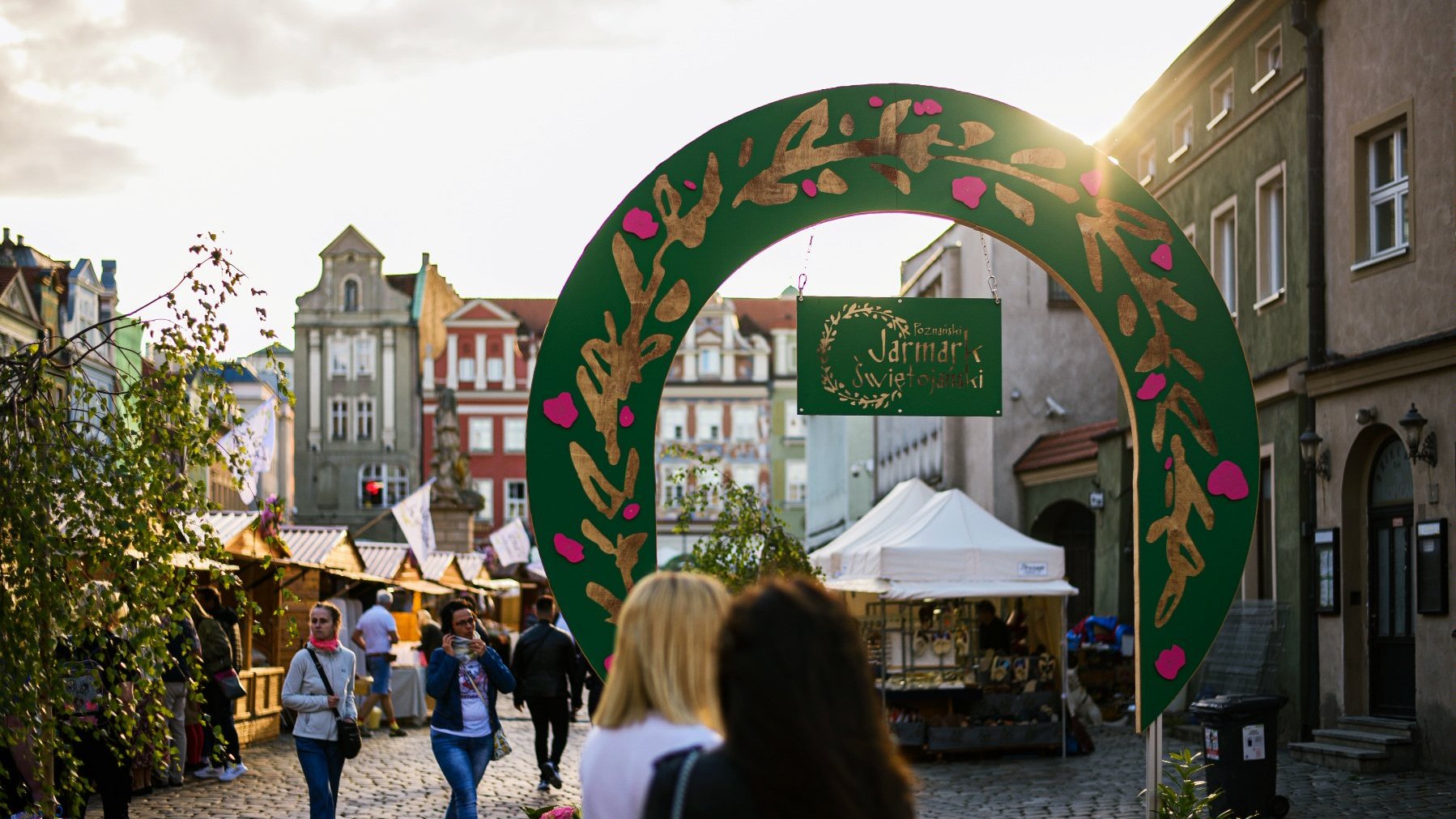 Galeria zdjęć przedstawia tłum ludzi na rynku podczas jarmarku i drewniane domki i stragany z różnymi towarami.