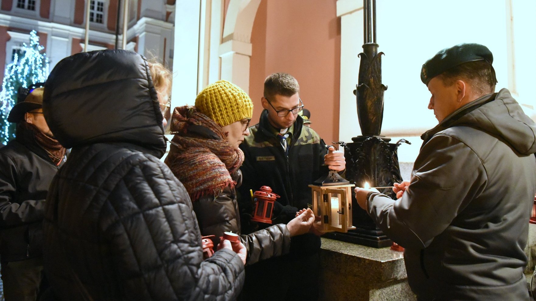 Na zdjeciu ludzie, którym przekazywane jest światło do lampionów