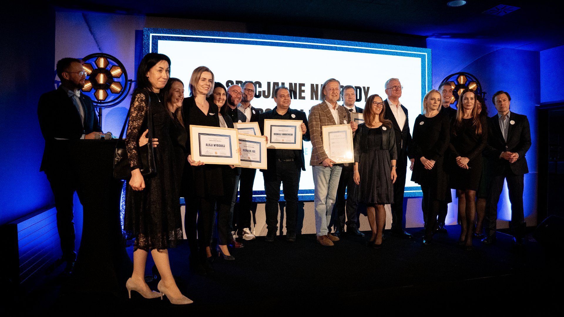 A group of people honoured by the Investor Relations Department with awards. They stand on stage, all dressed in evening wear.