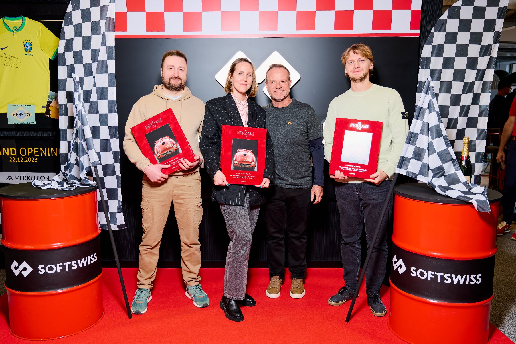 Rubens Barrichello is posing with three people on a wall holding books. In the background, elements of the décor relate to racing. - grafika artykułu