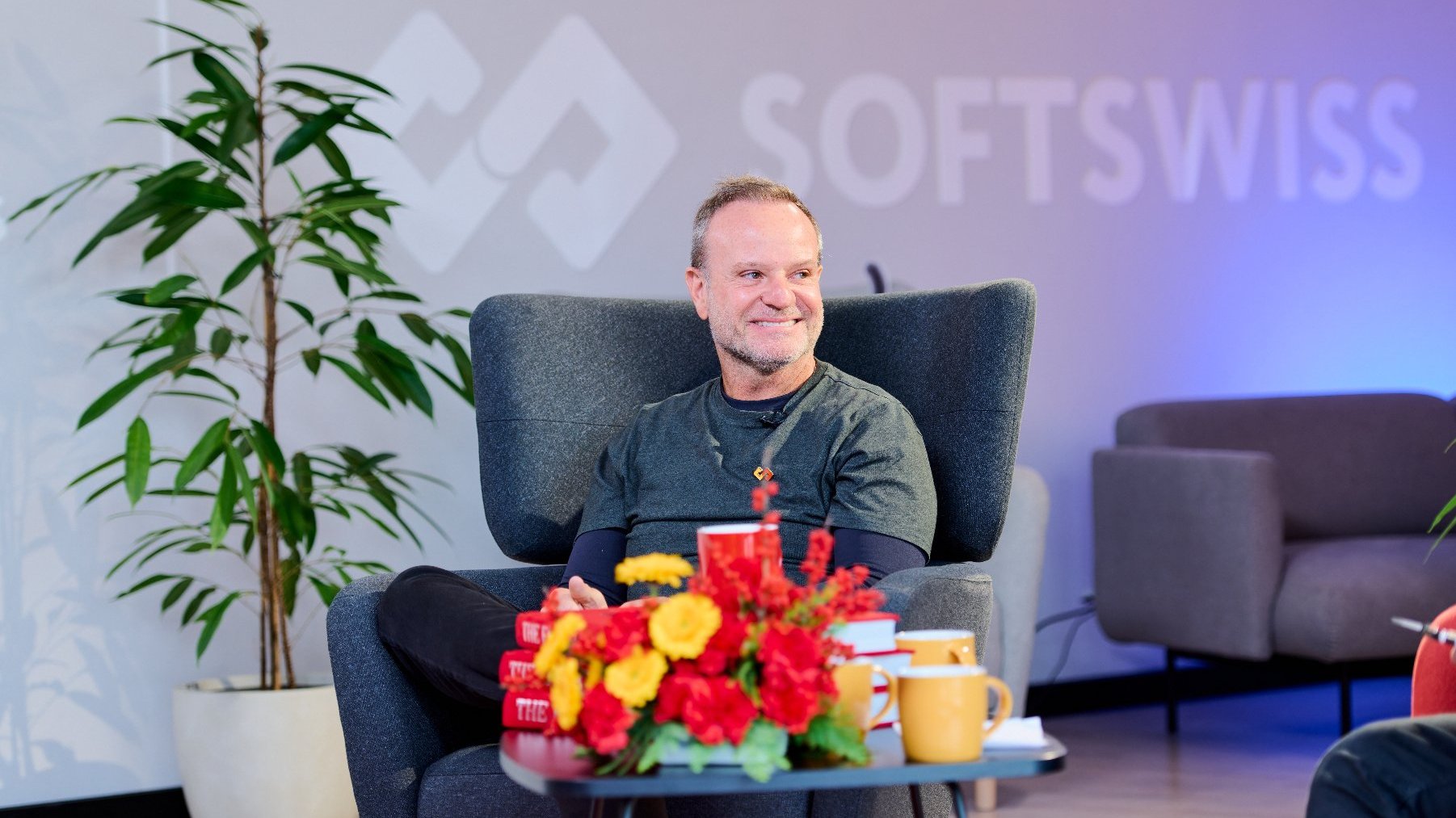 The photo shows a smiling Rubens Barrichello. He is seated in the chair.