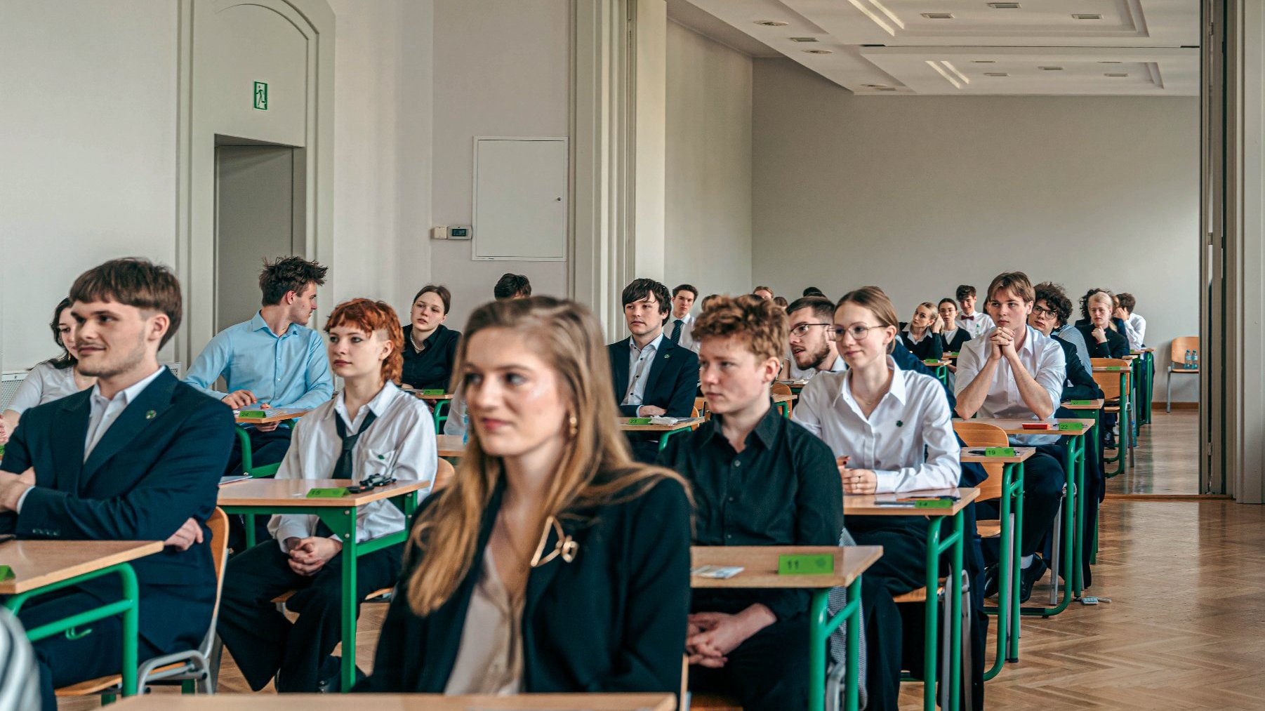 Zdjęcie przedstawia maturzystów siedzących w ławkach.