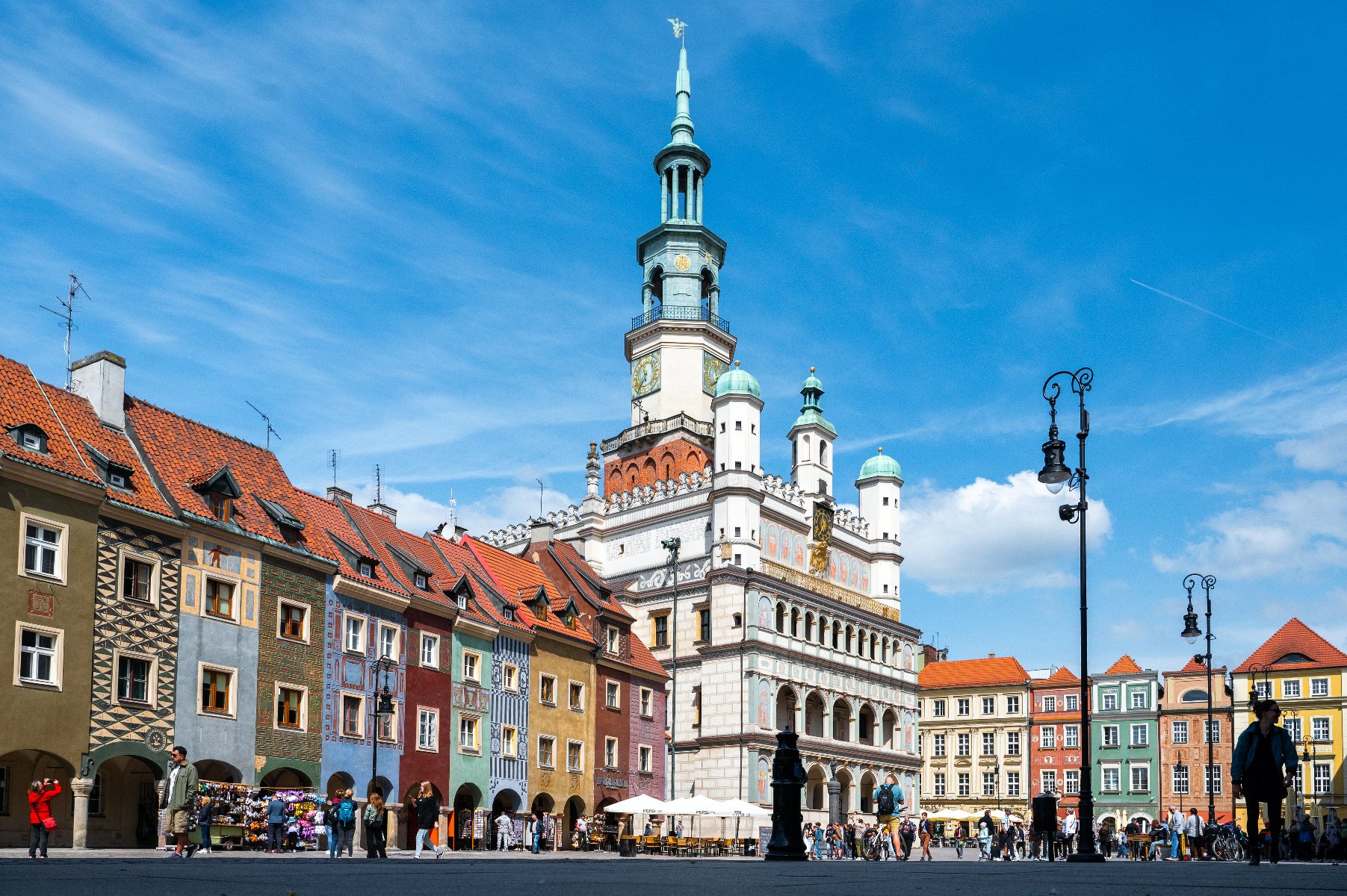 Zdjęcie przedstawia Stary Rynek w Poznaniu. W centralnej części kadru widać ratusz i domki budnicze, przed którymi przechadzają się mieszkańcy. - grafika artykułu