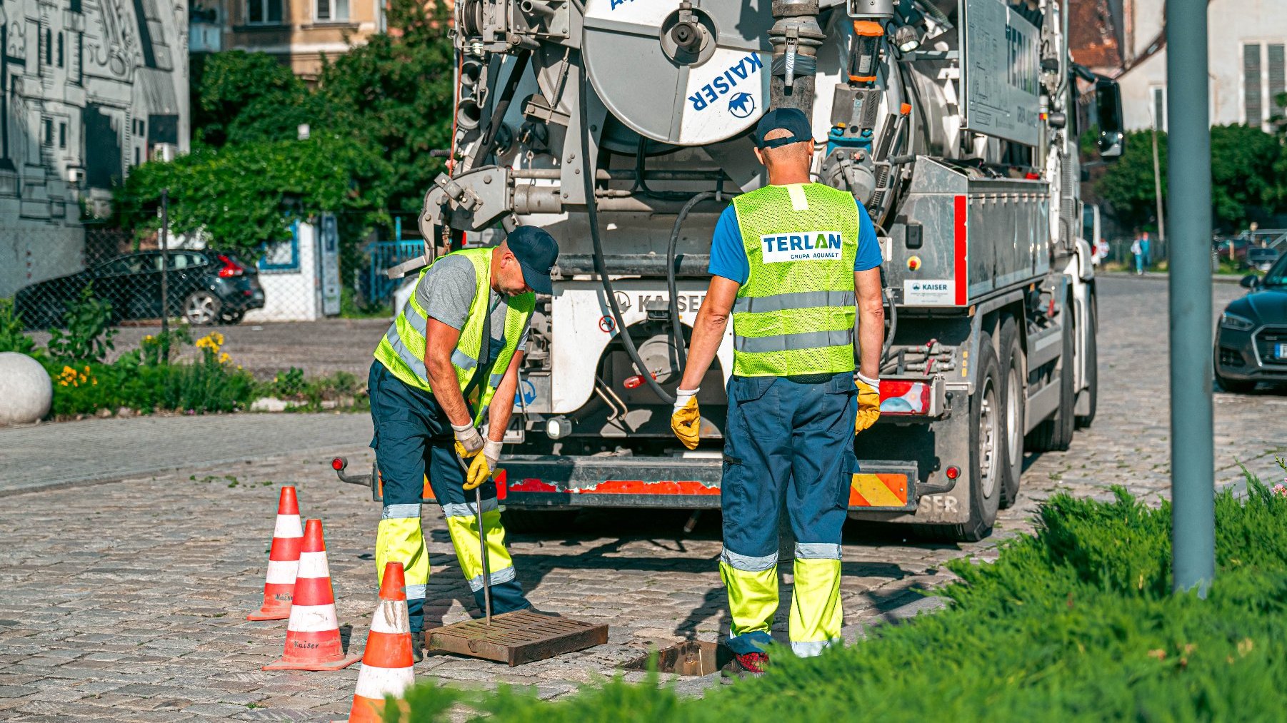 Zdjęcie przedstawia ludzi i specjalistyczny samochód podczas czyszczenia studzienek.