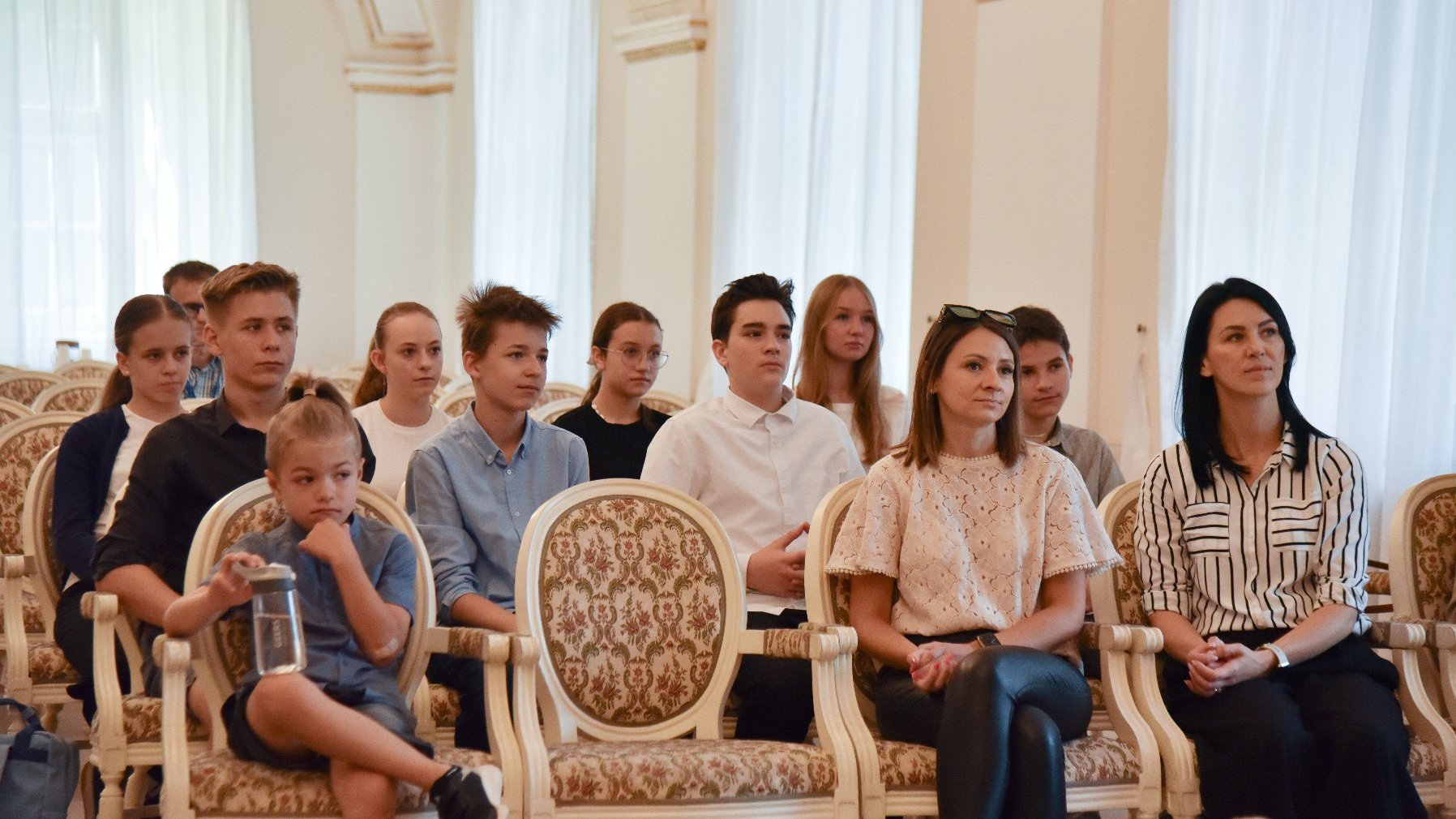 Na zdjęciu dzieci i dorośli siedzący w sali białej urzędu