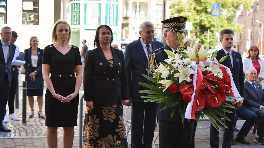 Na zdjęciu delegacja osób składających kwiaty pod tablicą