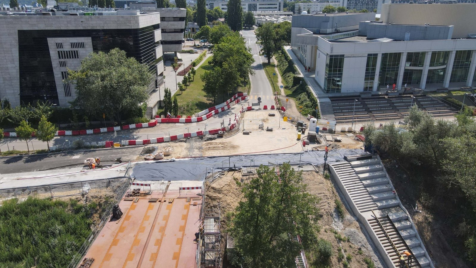 Zdjęcie przedstawia plac budowy i otaczające go budynki.