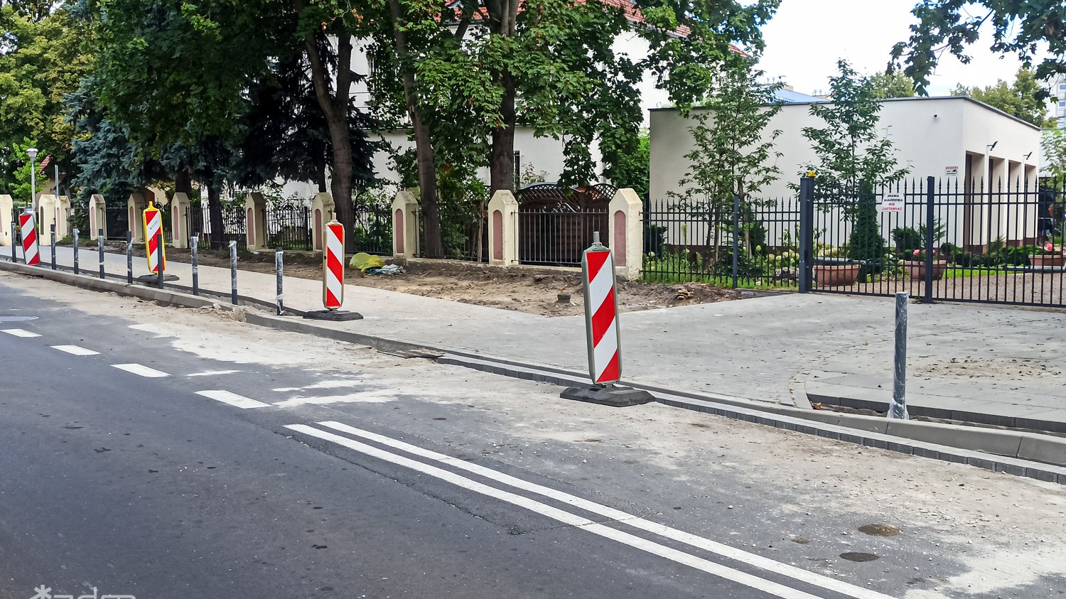 Zdjęcie przedstawia chodnik i jezdnie. W tle drzewa.