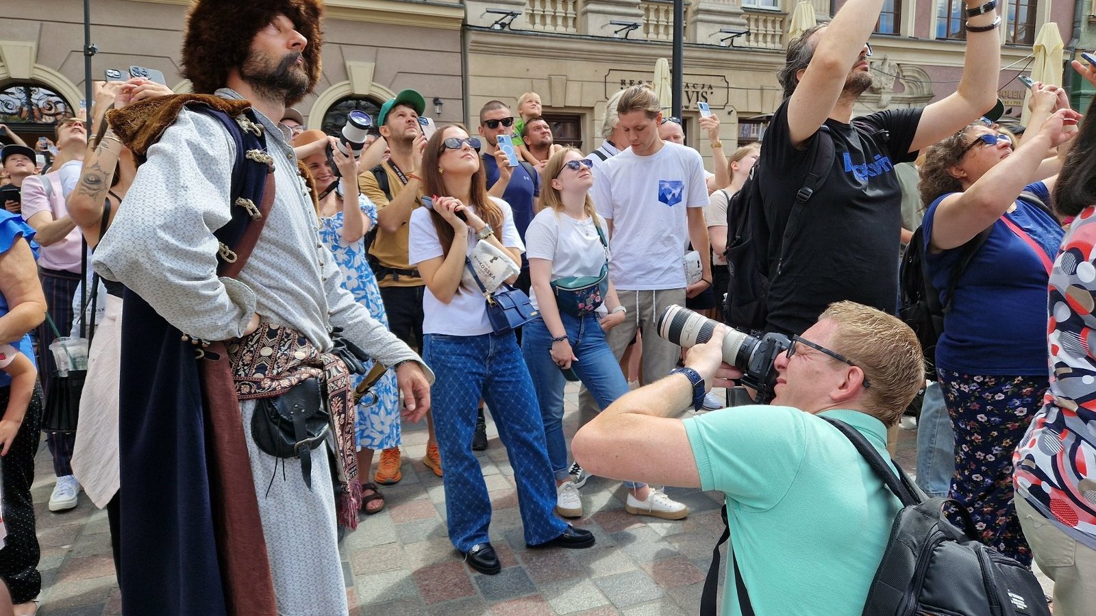 Na zdjęciu grupa ludzi na Starym Rynku, patrzą w górę, obok stoi przewodnik ubrany w historyczny strój