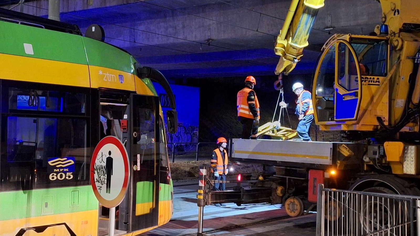 Zdjęcie przedstawia zepsuty tramwaj oraz maszynę i ludzi, którzy będą go holować lub naprawiać.