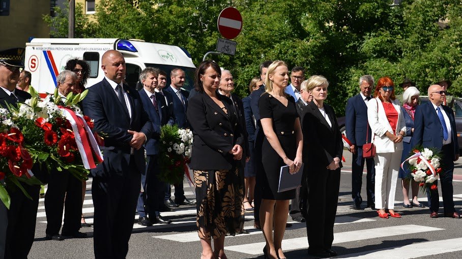 NA zdjeciu uczestnicy uroczystości stojący przed tablicą