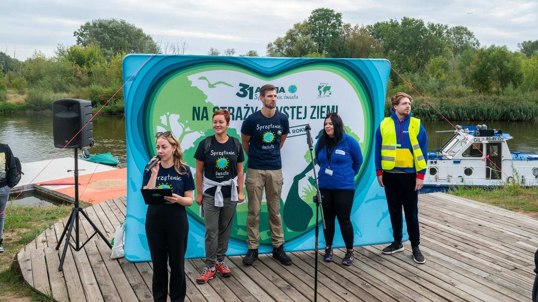 Zdjęcie przedstawia ludzi na podeście mówiących do mirofonu na tle Warty.