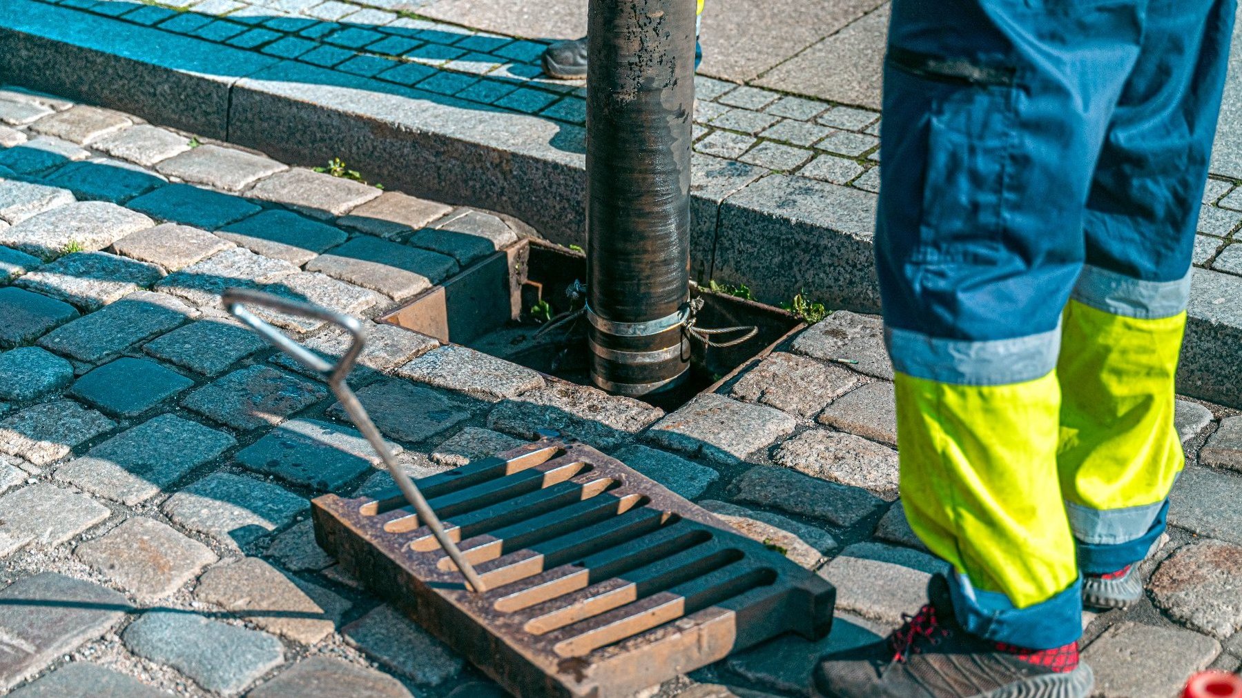 Zdjęcie przedstawia mężczyznę czyszczącego studzienkę. Widać tylko jego nogi.