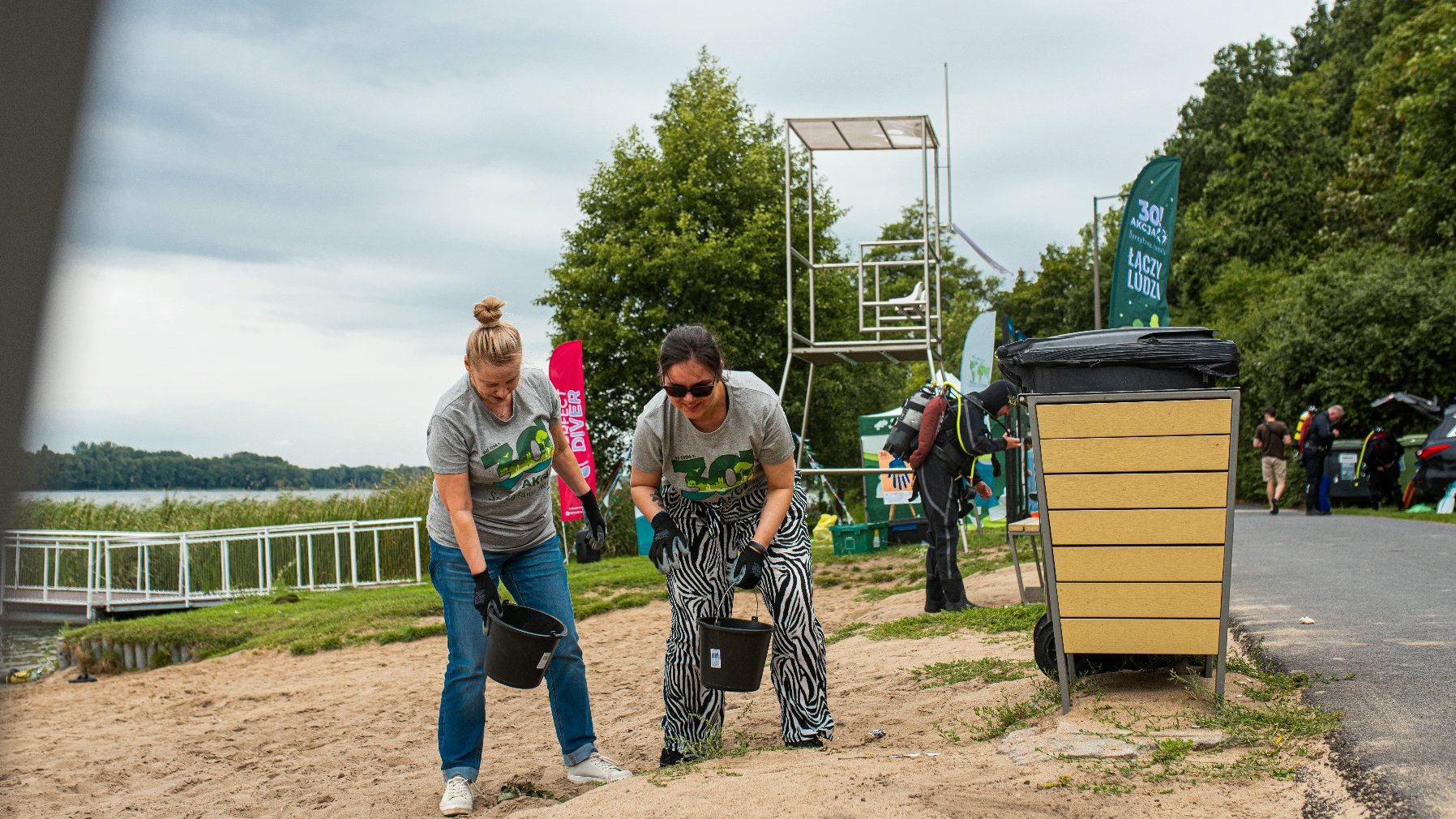 Zdjęcie przedstawia dwie kobiety sprzątające plażę.