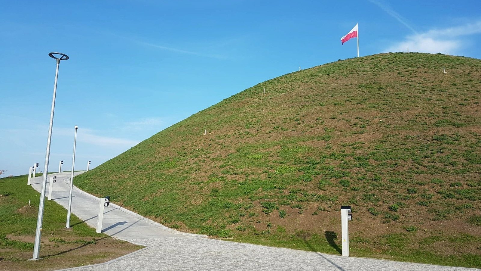 Zdjęcie przedstawia Kopiec Wolności i zwiedzajacych go ludzi.