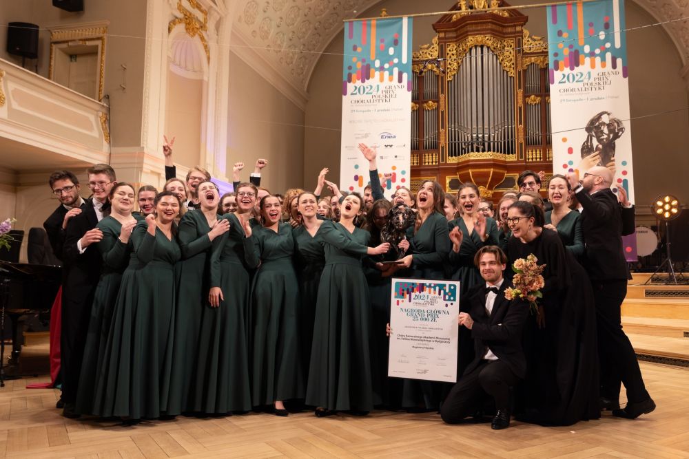 Grupa młodych ludzi stoi na scenie świętując zwycięstwo. Wszystkie twarze wyrażają radość i ekscytację. Kobiety mają na sobie wieczorowe, zielone suknie, mężczyźni - garnitury. - grafika artykułu