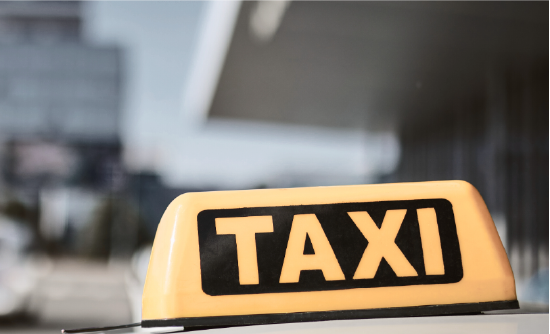 Licencja na taksówkę w Poznaniu Żółty znak taxi na dachu taksówki, w tle widoczna miejska ulica.