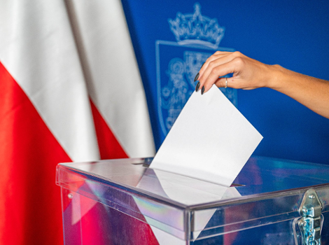Już w niedzielę odbędzie się druga tura wyborów Prezydenta RP Na zdjęciu dłoń wrzucająca głos do urny, w tle dwie flagi Polski
