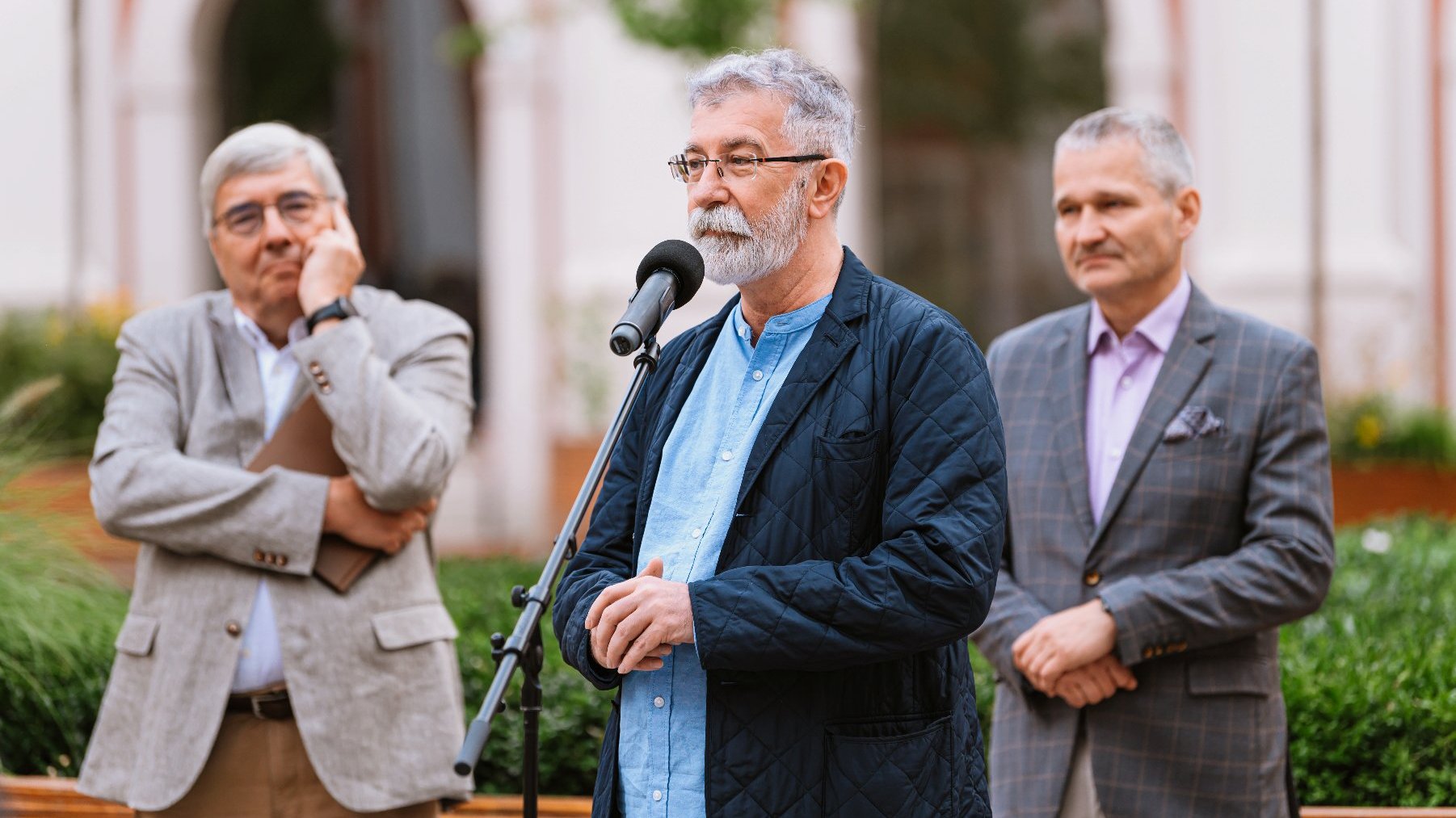 Na zdjęciu trzej mężczyźni, jeden z nich mówi coś do mikrofonu