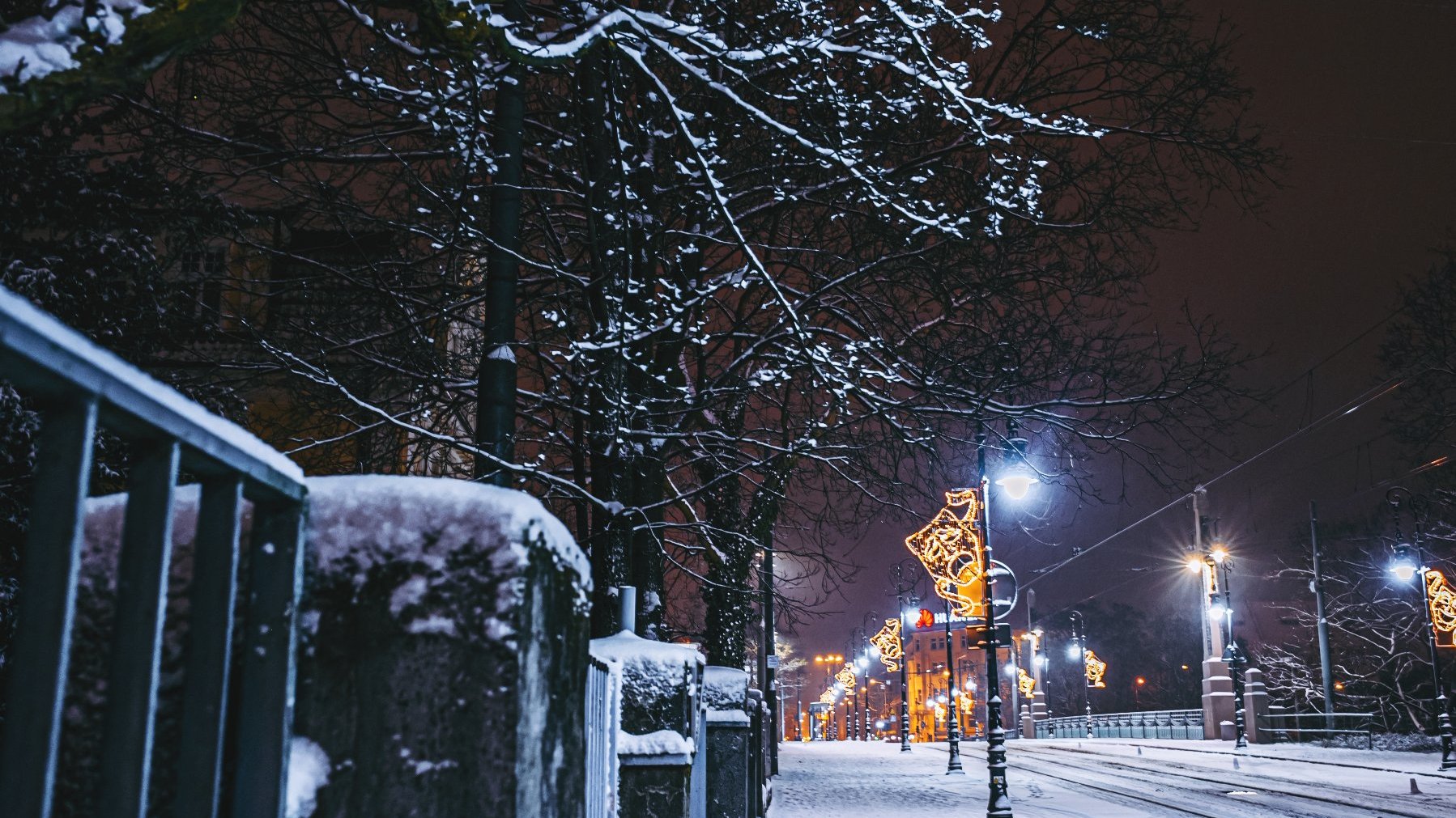 Zdjęcie przedstawia ulicę pokrytą śniegiem. Na latarniach zamontowane są iluminacje.